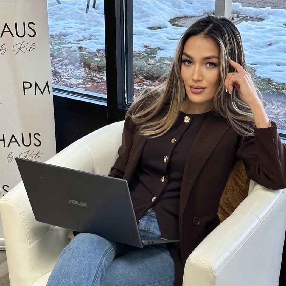 Woman in a brown blazer sits in a white armchair using an ASUS laptop.