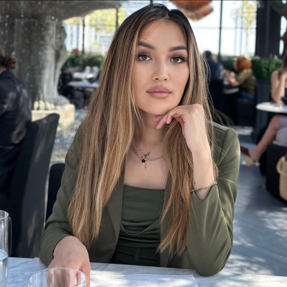 Woman with long highlighted hair in olive green blazer, resting her chin on her hand.
