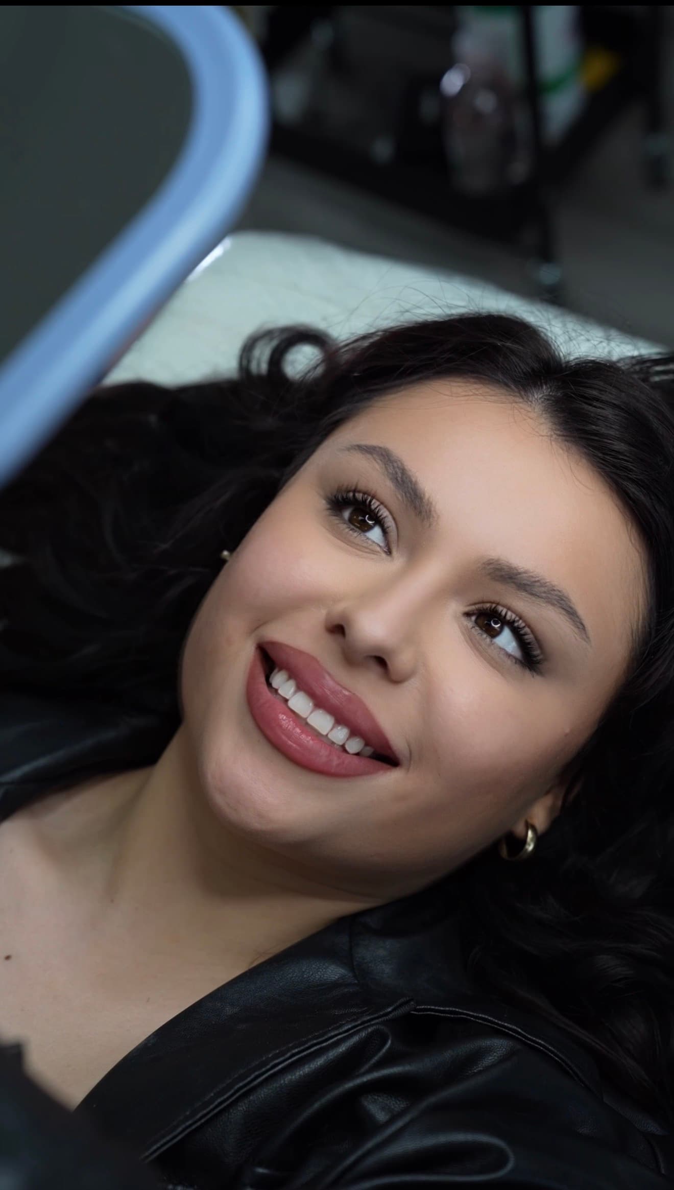 Smiling young woman with dark wavy hair and makeup looking up while lying down.