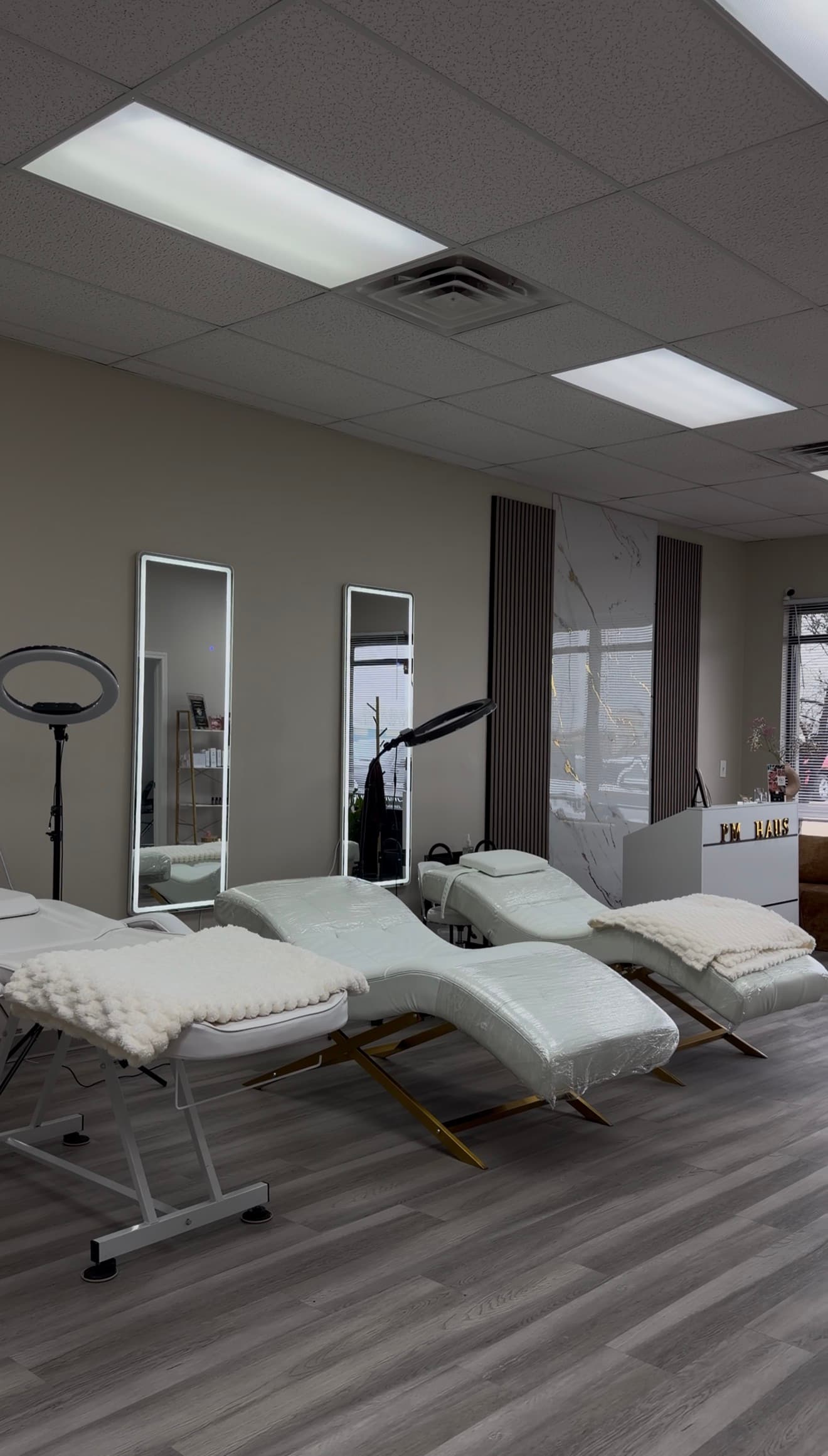 Modern beauty studio featuring white treatment beds, ring lights, and tall mirrors with gold accents.